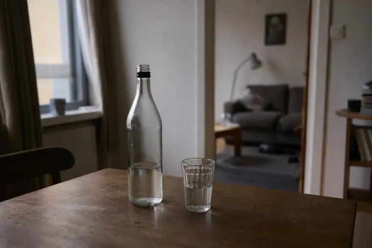 Merkitsemätön lasipullo ja juomalasi pöydällä vaatimattomassa olohuoneessa.